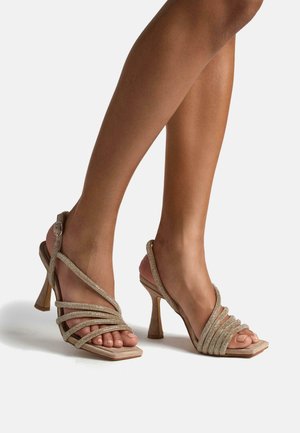 Sandalias de tacón alto beige con tiras, acentos brillantes, diseño de punta cuadrada y un tacón delgado, que cuentan con una correa de tobillo segura.