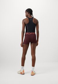 Black athletic tank top with pink accents, paired with maroon shorts featuring "PROPR" logo on the waistband. White socks and multi-colored sneakers.