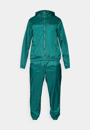 Teal tracksuit made of shiny synthetic material, featuring a zip-up jacket with a hood and matching elastic waistband pants. Black logo detail.