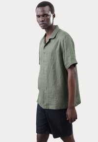 Groene linnen shirt met korte mouwen, een losse pasvorm, kraag en knoopsluiting, gecombineerd met zwarte shorts.