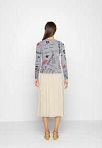 Haut à manches longues gris avec plusieurs phrases écrites à la main et des empreintes de lèvres, associé à une jupe plissée beige.