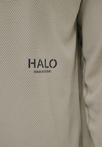 Beiger strukturierter Stoff mit einem Netzmuster, auf dem das Wort "HALO" und die Jahre "1968 1972 1981" in Dunkelblau gedruckt sind.