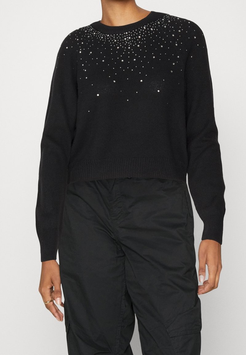 Pull court à manches longues noir avec de petites clous argentés dispersés sur la poitrine supérieure et pantalon cargo noir taille haute.