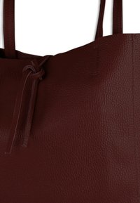 Bordeauxrode leren totebag met een gestructureerde afwerking, voorzien van een gestrikte sluiting en stevige schouderbanden. Eenvoudig en praktisch ontwerp.