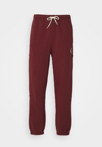Burgunderfarbene Sweatpants mit einem elastischen Bund, weißen Kordeln und gerippten Bündchen. Verfügt über Seitentaschen und ein Logodetail.