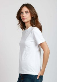 T-shirt bianca a maniche corte realizzata in cotone morbido, con scollatura a girocollo e un design semplice e privo di decorazioni. Indossata con jeans di denim blu.