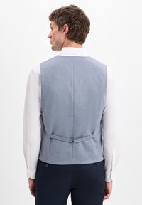 Helles blaugraues, strukturiertes Weste mit verstellbarem Rückengurt, getragen über einem weißen Hemd. Verfügt über ein figurbetontes Design, das eine klare, maßgeschneiderte Silhouette zeigt.