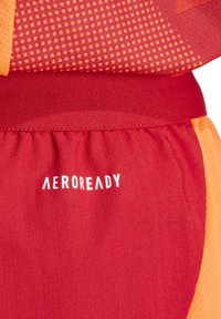 Rode en oranje sportshorts van een textuurstof, met gestreept ontwerp en "AEROREADY" branding in het wit op de tailleband.