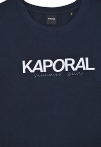 Granatowa bawełniana koszulka z białym logo "KAPORAL" napisanym pogrubioną czcionką oraz kursywą "Summer Sun" poniżej. Okrągły dekolt i krótkie rękawy.
