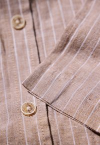 Brunrandig tyg med fina vita linjer, med en knappdetalj vid kragen. Texturen ser vävd och något grov ut.