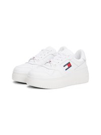 Tenis brancos com um cabedal de couro liso, biqueira redonda, sola grossa de borracha branca e um patch de logotipo com detalhes em vermelho e azul.