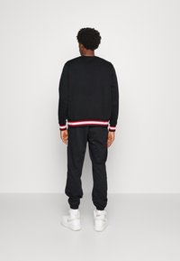 Conjunto de sudadera negra y pantalones jogger con detalles de rayas blancas y rojas en los puños y la cintura, combinado con zapatillas blancas.