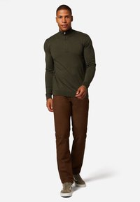 Donkergroene zip-halstrui, slim fit. Gecombineerd met bruine slim-fit broeken en grijze sneakers. Glad textuur, minimalistisch ontwerp.