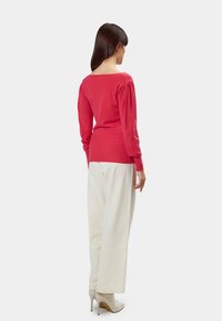Maglione rosso a maglia con maniche lunghe, corpo aderente e scollatura rotonda, abbinato a pantaloni bianchi larghi e tacchi alti beige.