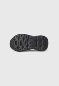 Semelle de chaussure en caoutchouc noir avec une surface texturée, dotée de découpes circulaires et ovales pour plus de flexibilité et d'adhérence.