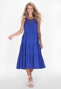 Rochie maxi fără mâneci, de un albastru regal, cu un design în straturi, dantelă decorativă la bust și o siluetă fluidă. Accentuata cu încălțăminte cu curele.