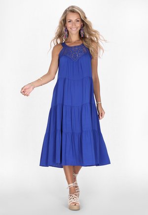 Königsblaue, ärmellose Maxikleid mit gestuftem Design, dekorativer Spitze im Oberteil und fließender Silhouette. Akzentuiert mit Riemchenschuhen.