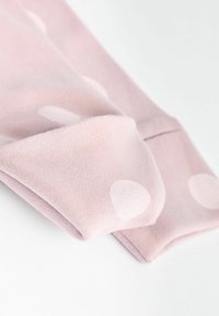 Világos rózsaszínű textil közeli képe, lágy textúrával és fehér pöttyökkel. Az anyag hajtva van, bőrén sima felület és tiszta él látható.