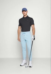 Camisa polo preta, calças de moletom azul claro e ténis brancos. Um boné azul e um taco de golfe acrescentam detalhe ao conjunto atlético. Tecido elástico.