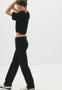 T-shirt noir cropped et jeans droits noirs. La tenue présente un design décontracté avec une texture lisse et un style minimaliste.