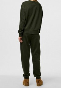 Completo felpa scura e pantaloni della tuta, realizzato in tessuto morbido con una vestibilità rilassata. Presenta polsini e vita a costine. Stivali marroni completano l'outfit.