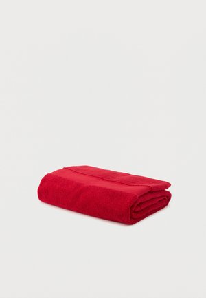 Serviette en coton rouge soigneusement pliée sur un fond blanc uni.