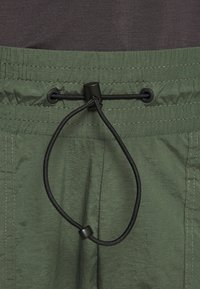 Pantalon vert avec taille élastique et cordon noir ajustable avec fermeture à bascule en plastique.