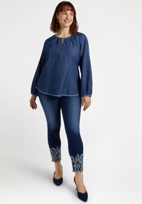 Denim-paita, jossa on löysä kaula-aukko ja avainreikäyksityiskohta, yhdistettynä istuviin farkkuihin, joiden helmassa on brodeerattuja paisley-akkentteja.