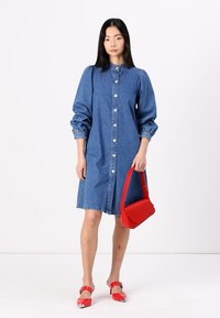 Denim dress, button-down front, round collar, puffed sleeves. Red handbag, square shape, smooth texture. Red heeled sandals with pointed toes.