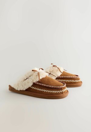 Brown suede slippers with cream faux fur trim, decorative woven accents, tied bows, and rounded shapes for comfort and warmth.