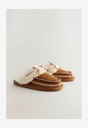 Brūnas zamšādas čības ar krēmkrāsas mākslīgā kažokāda apdari, dekoratīvām austām detaļām, sasietiem lokiem un noapaļotām formām ērtībai un siltumam.