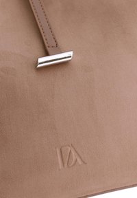 Bolso de mano de ante marrón con textura suave, un elegante detalle de hardware plateado y un logo en relieve en la superficie.