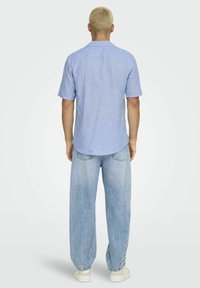 Lichtblauw shirt met korte mouwen van een textuurstof, gecombineerd met losvallende lichtblauwe jeans en witte sneakers. Achteraanzicht.