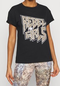 Una camiseta negra con el texto "REBEL GIRLS" en un patrón de estampado de leopardo, con un acento de estrella plateada, de mangas cortas y un corte relajado.