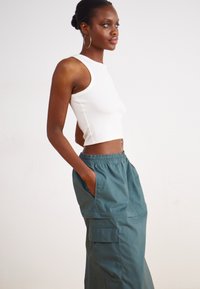 Fehér, rövidített ujjú tank top és laza zöld cargo nadrág oldalsó zsebekkel, elasztikus derékkal és puha tapintással.