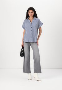 Striped button-up shirt in navy and white, short sleeves, paired with light grey wide-leg jeans, white heeled boots, and a small black handbag.