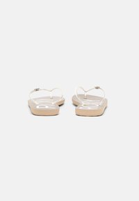 Sandales tongs blanches avec des brides transparentes et une semelle à texture boisée. Arbore un logo audacieux sur chaque semelle intérieure dans une couleur contrastante.