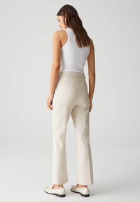 Witte mouwloze top gecombineerd met lichtbeige broek. De broek heeft achterzakken en een rechte pijp ontwerp. Schoenen met zwarte zolen.