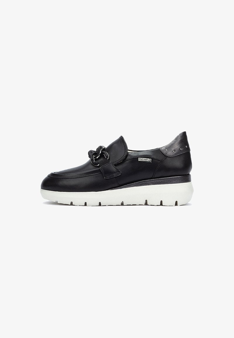 Chaussure noire en cuir à enfiler avec un accent chaîne à l'avant, semelle blanche rembourrée, forme arrondie et détails métalliques au talon.