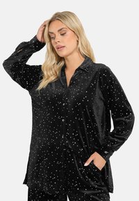 Camicia in velluto nero con motivo a stelle argentate, maniche lunghe, chiusura frontale con bottoni e tasche laterali. Tessuto morbido, vestibilità comoda.