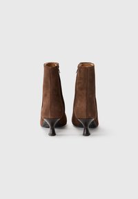 Botas de tobillo de ante marrón con un diseño elegante, que presentan una punta redonda y un tacón de aguja de altura media, con cierre de cremallera lateral.
