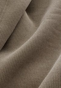 Bež ribareline kangas pehme tekstuuriga, millel on vertikaalsed jooned ja peened laigud, luues sooja ja kutsuva ilme.