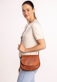 Pruun nahast õlakott kumerate ülemiste servadega, kuldse tooniga riistvara ja reguleeritava rihmaga. Sile tekstuur ja lihtne, kaunistusteta disain.