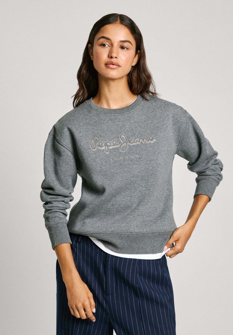 Felpa grigia con polsini e orlo a costine, caratterizzata da logo ricamato "Pepe Jeans London" in grigio chiaro, indossata sopra una camicia bianca.