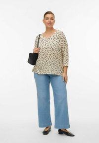 Haut beige à imprimé animalier noir, col en V, manches trois quarts, associé à un jean bleu clair à jambes larges, et chaussures plates noires.