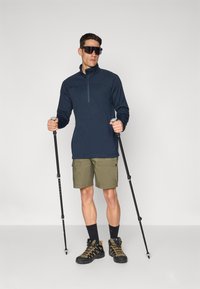 Marine kvart-zip top, olivgrønne cargo shorts, sorte vandrestøvler med orange accenter og trekkingstave. Glat stof og praktisk design.