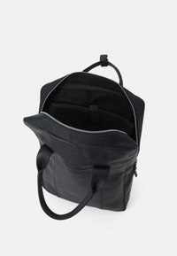 Zwarte leren tote bag met een rits bovenkant, voorzien van twee handvatten en een binnenvak. Gladde textuur en minimalistisch ontwerp.