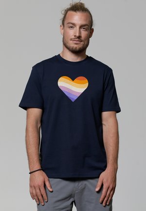 Dunkelblaues Baumwoll-T-Shirt mit einem mehrfarbigen Herzgrafik, das horizontale Streifen in Orange, Lila und Creme zeigt. Kurze Ärmel, Rundhalsausschnitt.