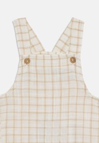 Pichones y white overalls de cuadros hechos de tela ligera, con tirantes ajustables y acentos de botones de madera.