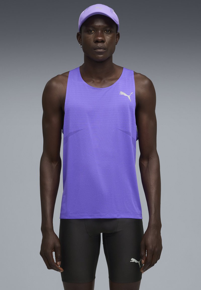 Camiseta atlética sin mangas de color púrpura, hecha de un tejido transpirable, combinada con pantalones cortos negros. Presenta el logo de Puma y un corte estructurado.